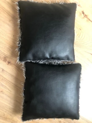 Caesar kuddar med konstläder och fuskpäls - Två snygga kuddar från Caesar med svart konstläder på ena sidan och grå fuskpäls på andra. Kuddarna är fyrkantiga och har en modern look som passar perfekt som inredningsdetalj i soffan eller sängen. Kommer i originalförpackning.