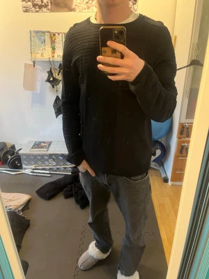 Svart stickad tröja från S.C.W. - Säljer en svart stickad tröja från S.C.W. med rund halsringning och diskreta ribbade detaljer upptill. Tröjan har lång ärm och en enkel, clean look som passar till det mesta. Perfekt för dig som gillar stilrena plagg med en modern touch.