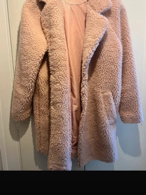 Beige teddyjacka  - Mysig teddyjacka i beige med stora slag och två sidofickor. Jackan har en oversized passform och är fodrad på insidan för extra komfort. Perfekt för kalla dagar och ger en trendig look. Materialet är fluffigt och mjukt, vilket gör jackan superbekväm.