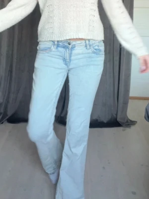 Ljusblå bootcut jeans - Säljer ett par ljusblå bootcut jeans med låg midja och klassiska fem fickor. Jeansen har en avslappnad passform och är tillverkade i denim med lätt tvättad look. Perfekta för en casual och trendig stil.