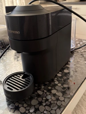 Svart Nespresso kaffemaskin DeLonghi - Säljer en stilren svart Nespresso kaffemaskin från DeLonghi. Maskinen har en modern design med rundade former och tydlig logga framtill. Avtagbar droppbricka och vattenbehållare baktill. Perfekt för dig som vill ha snabb och god kaffe hemma.