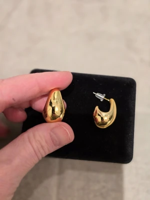Guldpläterade droppformade örhängen - Säljer ett par coola droppformade örhängen i guldpläterat metall. De har en blank och glansig finish som verkligen sticker ut. Perfekt för dig som gillar statement-smycken och vill ha något unikt i smyckeslådan.