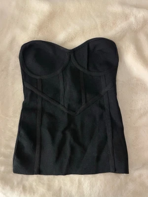 Svart bustier body utan axelband - Snygg svart bustier body med markerade sömmar och vadderade kupor. Axelbandslös design som ger en clean och stilren look. Tillverkad i stretchigt material som formar sig efter kroppen. Perfekt att styla under en skjorta eller kavaj.