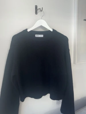 Svart stickad tröja från Bershka - Mysig svart stickad tröja från Bershka med rund halsringning och långa ärmar. Tröjan har en lätt luddig yta och ribbstickade muddar vid halsen. Perfekt för kalla dagar och enkel att matcha med olika outfits.
