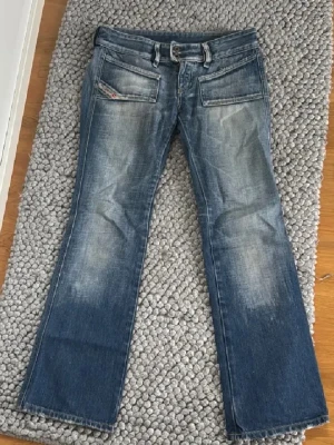 Blå bootcut jeans - Säljer ett par blå bootcut jeans. Jeansen har låg midja. Storlek w27, midjemåttet rakt över : 39cm och innerbens längden : 73cm. Dom e ganska tajta precis vid låren och måttet vid låren är 20 cm rakt över. Defekter förekommer.Hör av er vid några funderingar!