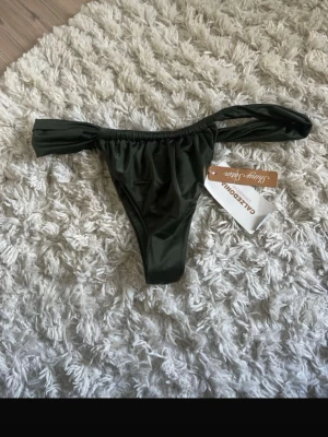 Mörkgrön bikiniunderdel Calzedonia - Snygg mörkgrön bikiniunderdel från Calzedonia med breda sidopartier och elastisk midja. Tillverkad i ett glansigt syntetmaterial som ger en modern look. Perfekt för strand eller poolhäng.
