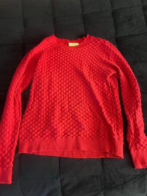 Röd stickad tröja med strukturmönster - Säljer en röd stickad tröja med coolt strukturmönster över hela plagget. Tröjan har rund halsringning, långa ärmar och ribbade muddar vid ärmslut och nederkant. Perfekt för dig som vill ha något färgglatt och bekvämt i garderoben.
