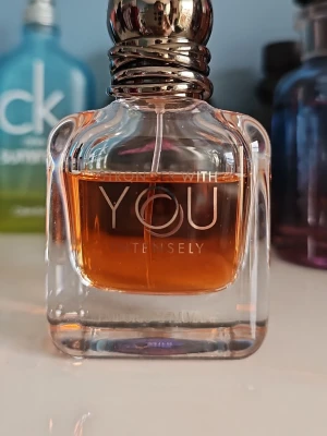 Emporio Armani Stronger With You Intensely - En elegant parfymflaska från Emporio Armani, Stronger With You Intensely. Flaskan är genomskinlig med rundade former och har en varm bärnstensfärgad vätska. Locket är metalliskt och stilrent. Perfekt för dig som gillar exklusiva dofter.