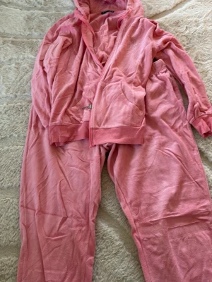 Rosa mjukisdress med huva - Säljer en supermjuk rosa loungewear-set i velour med dragkedja, huva och fickor på tröjan samt matchande byxor med dragsko i midjan. Perfekt för chill dagar hemma eller när du vill vara extra bekväm.