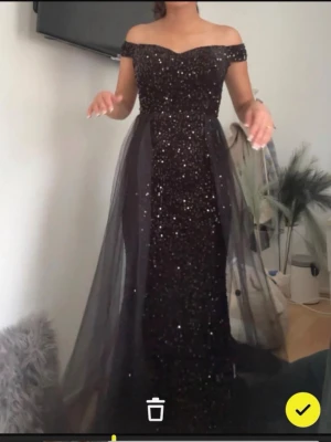 Svart glittrig långklänning offshoulder - Säljer en svart långklänning med glittriga paljetter och offshoulder-modell. Klänningen har ett lager av tunn tyll över kjolen som ger extra volym och en elegant look. Perfekt för bal eller festliga tillfällen.