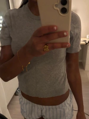 Ljusgrå ribbad topp - Säljer en ljusgrå ribbad topp med rund hals och korta ärmar. Toppen är figurnära och har en enkel, stilren design som passar till det mesta. Materialet ser ut att vara mjukt och stretchigt, perfekt för en avslappnad look.