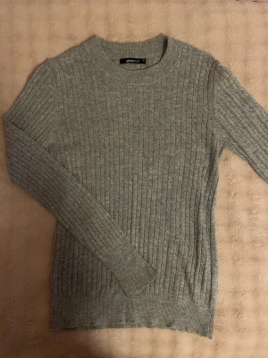Grå ribbstickad tröja Gina Tricot - Säljer en stilren grå ribb stickad tröja från Gina Tricot. Tröjan har rund halsringning, långa ärmar och är gjord i mjukt material som passar perfekt till lager på lager. Enkel och snygg design som funkar till det mesta.