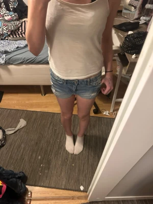 Blå jeansshorts med slitningar - Säljer ett par klassiska blå jeansshorts i denim med slitna detaljer och råa kanter. Shortsen har fem fickor och knappgylf. Perfekta för sommaren och ger en avslappnad look. Och man kan ha dom korta eller långa 
