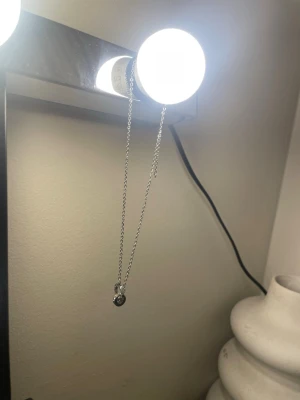 Silverfärgat halsband med cirkelberlock - Säljer ett stilrent silverfärgat halsband med tunn kedja och en rund cirkelberlock dekorerad med små stenar. I cirkeln hänger även en liten nyckelberlock. Perfekt accessoar för dig som gillar minimalistisk och trendig stil. Nyttt från Edblad 