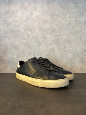 Axel Arigato Clean 90 - Säljer dessa Axel Arigato Clean 90 i läder med vit sula och vit detalj på hälen. Klassisk låg modell med svarta skosnören och diskret logga på sidan. Perfekta för en clean och stilren look. Vanligt slitage finns men fina i lädret!