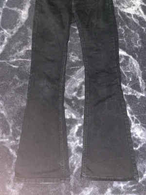 Svarta bootcut jeans - Säljer ett par svarta bootcut jeans med utsvängda ben. Jeansen har klassisk femficksdesign och är tillverkade i ett mjukt denimtyg. Perfekta för dig som gillar retrovibbar och vill ha en snygg siluett.