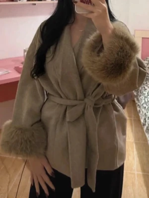 Khaki färgad kappa str M - Trendig beige kappa med breda ärmar och stora päls detaljer vid ärmsluten. Knytskärp i midjan ger en snygg siluett och kappan har en öppen design utan synliga knappar. Perfekt för dig som vill ha en chic och mysig look.