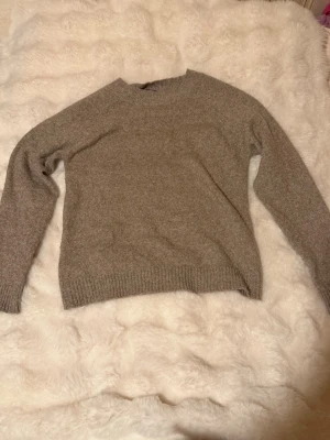 Beige stickad tröja Vero Moda - Mysig beige stickad tröja från Vero Moda med rund halsringning och ribbade muddar vid ärmslut och nederkant. Perfekt för lager på lager och enkel att matcha med olika outfits. Tillverkad i mjukt material som känns skönt mot huden. 