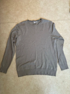 Grå tröja från Lindbergh - Snygg grå tröja från Lindbergh med relaxed fit. Tröjan har rund halsringning, långa ärmar och diskret Lindbergh-logga broderad på bröstet. Tillverkad i mjukt material som passar perfekt till olika stilar.