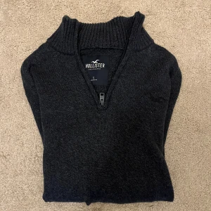 Mörkgrå stickad tröja Hollister - Snygg mörkgrå stickad tröja från Hollister med ribbad hög krage och half zip-dragkedja framtill. Tröjan har långärmad passform och diskret Hollister-logga på bröstet. Perfekt för dig som gillar klassisk och enkel stil. Skick 9,5/10