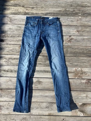 Blå raka jeans med slitningar - Säljer ett par klassiska blå jeans med rak passform och lätt slitna detaljer. Jeansen har fem fickor, normal midja och är gjorda i denim. Perfekta för en avslappnad och trendig look. Strl 29-32 