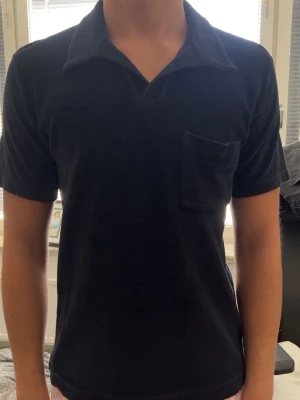 Mörkblå frotté t-shirt med krage - Säljer en mörkblå t-shirt i mjuk frotté med klassisk krage och bröstficka. T-shirten har korta ärmar och en relaxed passform som ger en chill vibe. Perfekt för dig som vill ha något annorlunda än vanliga bomullströjor. Använd fåtals gånger och säljer pga att  den är för liten! Ny pris-999kr/ mitt pris-300kr