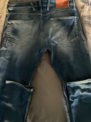 Blå jeans med tvättad look - Säljer ett par blå jeans med snygg tvättad effekt och raka ben. Jeansen har två bakfickor med dekorativa sömmar och klassisk femficksdesign. Passar perfekt till en avslappnad stil och har bälteshällor i midjan.