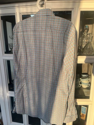 Rutig skjorta från Eton slim fit - Säljer en snygg rutig skjorta från Eton i slim fit. Skjortan har ett klassiskt rutmönster i blått, vitt och röda toner, lång ärm och krage. Perfekt för dig som gillar stilrena och tidlösa plagg. Materialet är mjuk bomull som känns skönt mot huden. Storlek 16(41) och strykfri.