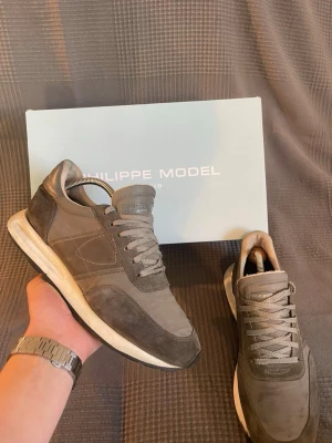 Philippe model - Snygga grå sneakers från Philippe Model med ovandel i mocka och textil. Skorna har vita sulor och klassisk snörning. Perfekta för dig som gillar stilrena och tidlösa sneakers med en sportig touch.