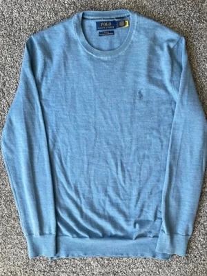 Blå merinoulltröja från Polo Ralph Lauren - Snygg ljusblå stickad tröja från Polo Ralph Lauren i tvättbar merinoull. Slim fit-modell med rund halsringning och diskret broderad logga på bröstet. Perfekt för dig som gillar klassisk och stilren design.