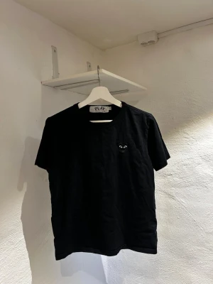 Svart Comme des Garçons PLAY t-shirt - Svart t-shirt från Comme des Garçons PLAY med det ikoniska hjärteögon-logotypen broderad på bröstet. Klassisk passform med rund hals och korta ärmar. Tillverkad i mjuk bomull som känns skön mot huden. Står L i men skulle säga att den passar S/M. 