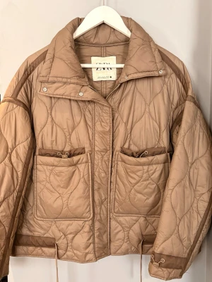 Brun quiltad pufferjacka från Zara - En brun quiltad tunn dunjacka från Zara. Jackan har stora framfickor, midjeband, hög krage och dragkedja med tryckknappar. Storleken är xs/ 36 men har en lite oversised passform och är en perfekt vårjacka. 🌸