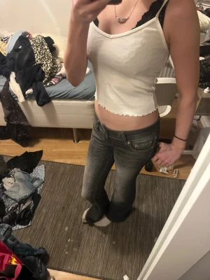 Vit ribbad linnetopp från H&M - Säljer en vit ribbad linnetopp från H&M med smala axelband och croppad passform. Toppen har en liten rosett framtill och vågig kant nertill för en söt touch. Perfekt till jeans eller kjol för en enkel och trendig look.