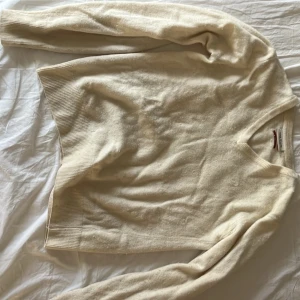 Beige stickad tröja med v-ringning - Klassisk beige stickad tröja med v-ringad hals och ribbade muddar vid ärmslut och nederkant. Perfekt att slänga på sig över en skjorta eller t-shirt. Tröjan har en enkel och stilren design som passar till det mesta.