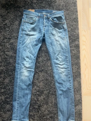 Dondup ljusblå - Säljer ett par ljusblå slim fit jeans med slitningar och klassisk femficksmodell. Jeansen har dragkedja och knapp i midjan samt detaljerade sömmar på bakfickorna. Perfekta för en avslappnad och trendig look.