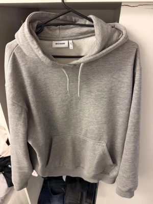 Grå hoodie från Weekday - Klassisk grå hoodie från Weekday med stor känguruficka framtill och justerbar dragsko i huvan. Tillverkad i mjukt bomullsmaterial för en skön och avslappnad look. Perfekt oversized passform och ribbade muddar vid ärmar och nederkant.
