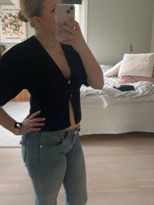 Svart croppad topp med knappar - Snygg mörkblå croppad topp med v-ringning och två dekorativa knappar framtill. Toppen har korta, vida ärmar och en loose passform som ger en avslappnad look. Perfekt att styla med jeans eller kjol för en trendig outfit.