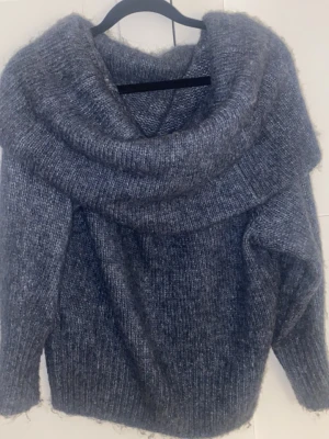 Grå stickad tröja från H&M - Mysig grå stickad tröja från H&M med stor polokrage och lång ärm. Tröjan har en fluffig och mjuk känsla, perfekt för kyliga dagar. Ribbstickad struktur och avslappnad passform gör den både trendig och bekväm.