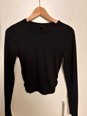 Svart långärmad topp från ONLY - En enkel och stilren svart långärmad topp från ONLY. Toppen har rund halsringning och är tillverkad i ett mjukt, ribbat material som sitter snyggt på kroppen. Perfekt att matcha med jeans eller kjol för en clean look.