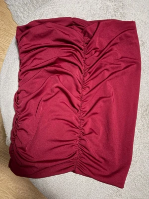Vinröd kjol med rynk från SHEIN - Säljer en vinröd kortkjol från SHEIN i storlek S. Kjolen har snygga rynkdetaljer framtill som ger en cool och trendig look. Perfekt att styla med en enkel topp eller stickad tröja. Materialet känns mjukt och följsamt.