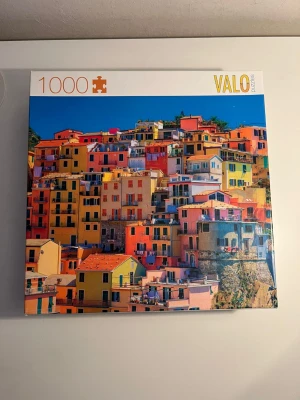 VALO 1000-bitar pussel färgglada hus - Säljer ett pussel från VALO med 1000 bitar. Motiv av färgglada hus staplade på en sluttning, inspirerat av italienska kuststäder. Pusselbitarna är av kartong och motivet har starka färger som gult, orange, blått och rosa. Perfekt för dig som gillar utmanande pussel och snygga motiv.