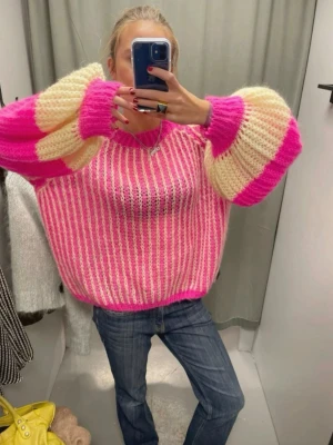 Rosa och vit stickad tröja med puffärm - Säljer en färgglad stickad tröja med breda ränder i rosa och vitt. Tröjan har oversized passform och stora puffärmar med breda ränder i rosa och cremevitt. Mjuk och luftig stickning, perfekt för dig som gillar statement-plagg. Helt ny skick och aldrig använd, saknar dock prislapp