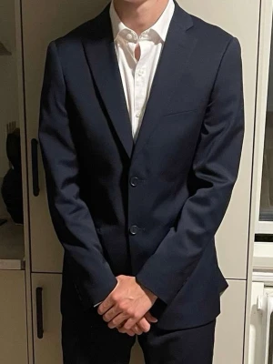 Mörkblå kostym med kavaj och byxor - Säljer en stilren mörkblå kostym med klassisk kavaj och matchande byxor från Dressman. Använd två gånger.