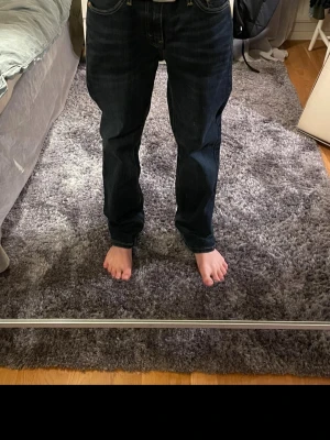 Mörkblå Levis jeans - Säljer ett par mörkblå Levi’s jeans i fint skick. Inte helt säker på exakt modell, men det står 541 i dem så det är nog modellen. Storlek: W30 L30. Passformen är ganska bekväm och lite mer åt det avslappnade hållet, inte supertight. Mörk tvätt som gör att de funkar både till vardags och lite mer uppklätt. Klassisk 5-ficksmodell och bra kvalitet som håller länge. Använda men fortfarande i bra skick, inga hål eller större slitningar vad jag kan se. Säljer eftersom de inte kommer till användning