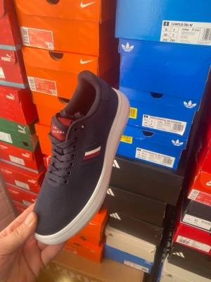 Marinblå sneakers Tommy Hilfiger - Snygga marinblå sneakers från Tommy Hilfiger med vit sula och klassisk logga i rött, vitt och blått på sidan. Skon har en låg profil, textilöverdel och svarta skosnören. Perfekt för dig som gillar stilrena och sportiga skor.