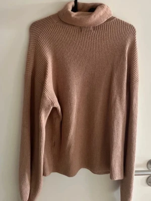 Beige polotröja från Donna Romina - Mysig beige stickad polotröja från Donna Romina x NA-KD. Tröjan har en hög polokrage, lång ärm och är ribbstickad för extra komfort. Perfekt för lager på lager och en avslappnad men snygg look.