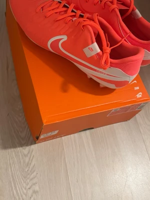 Nike Tiempo rosa fotbollsskor - Snygga fotbollsskor från Nike i modellen Tiempo. Skorna är i en stark rosa färg med vita detaljer och Nike-logga på sidan. De har klassisk snörning och är designade för bra grepp på planen. Perfekta för dig som vill sticka ut på matchen.