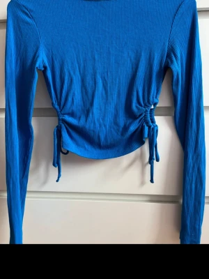 Blå ribbad topp med snörning - Snygg blå långärmad topp med ribbad struktur och trendig snörning i sidorna som ger en croppad look. Perfekt att styla med höga jeans eller kjol för en cool vibe.
