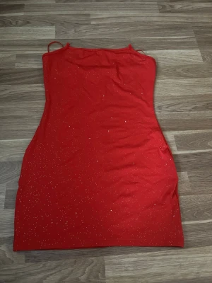 Röd glittrig kort klänning - Snygg röd kort klänning med tunna axelband och glittriga detaljer. Klänningen har en figurnära passform och är perfekt för dig som vill sticka ut. Materialet känns mjukt och stretchigt, vilket gör den bekväm att bära hela kvällen.