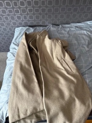 Beige ullkappa med fickor - Stilren beige kappa i ullmix med rak passform och diskreta sidofickor. Perfekt för dig som gillar minimalistisk och klassisk look. Kappan har enkel design utan synliga knappar och faller snyggt över kroppen.